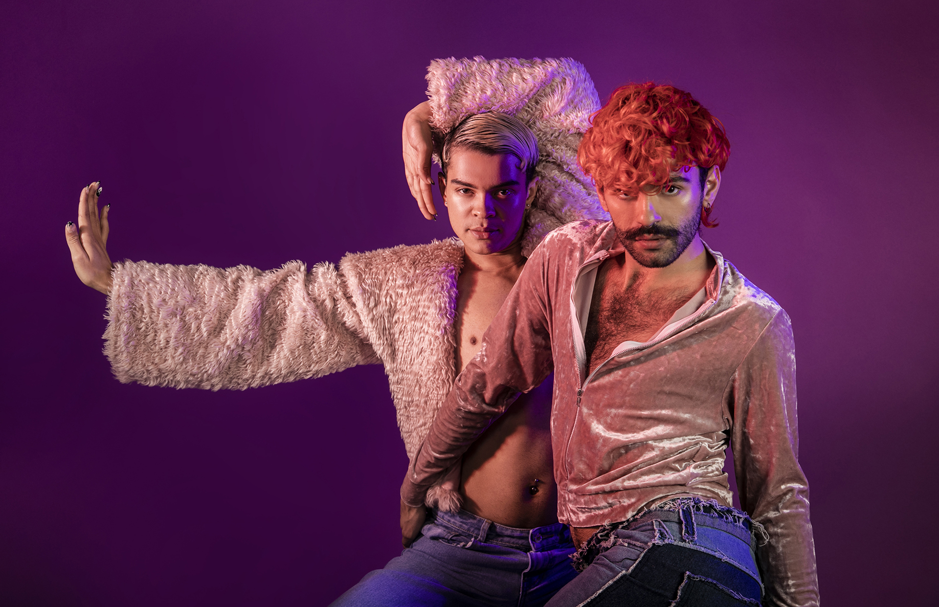 Two global majority LGBTQ+ male voguing dancers. Wearing pink tops and blue jeans on purple studio background. Two global majority LGBTQ+ male voguing dancers. Wearing pink tops and blue jeans on purple studio background.