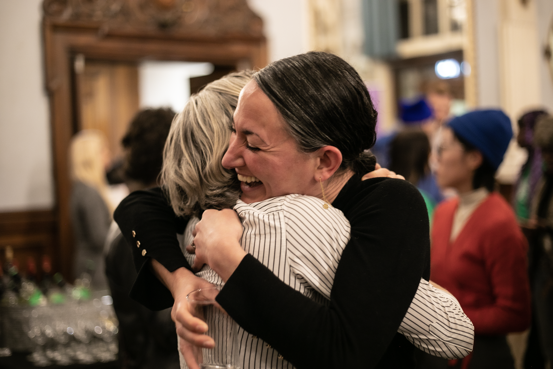 Two females hugging with big smiles with a crowded room
