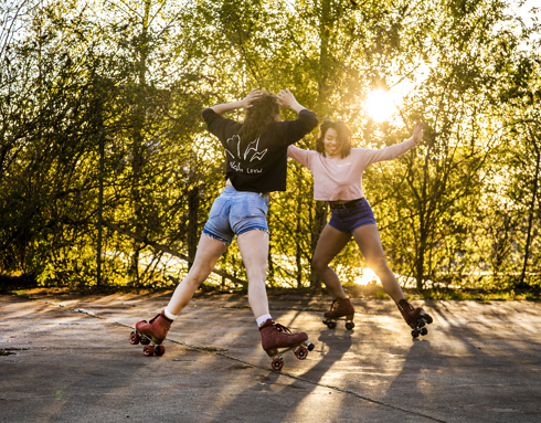 two female roller skaters skating around each other with smiles in golden dappled light with trees in the background two female roller skaters skating around each other with smiles in golden dappled light with trees in the background