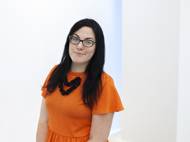 Headshot of Lara Coffey white female with black long hair and glasses smiling at the camera. Wearing orange top Headshot of Lara Coffey white female with black long hair and glasses smiling at the camera. Wearing orange top