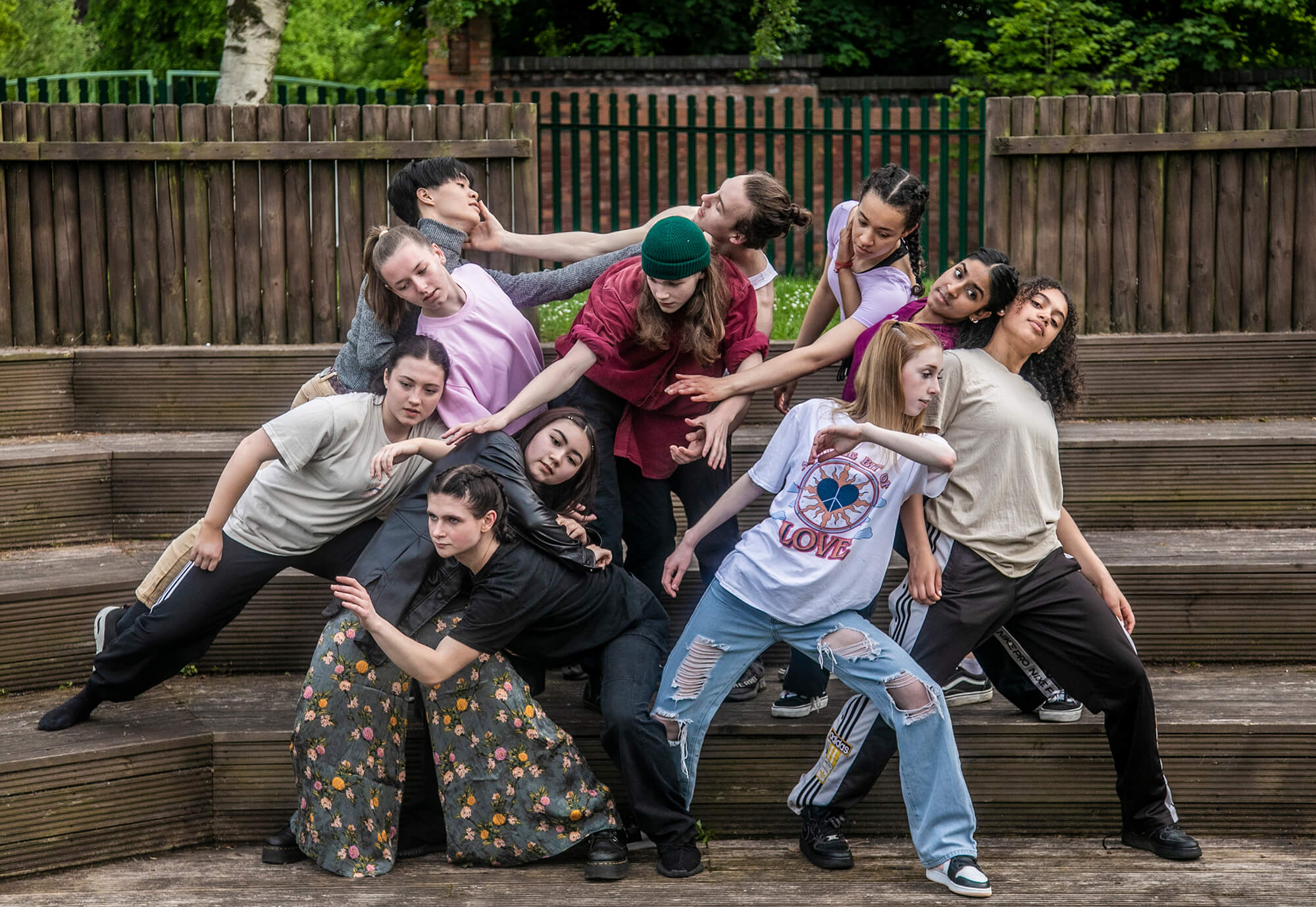 Eleven young male and female dancers huddled in a group on wooden steps moving around eachother with stretched arms. Causually dressed. Eleven young male and female dancers huddled in a group on wooden steps moving around eachother with stretched arms. Causually dressed.